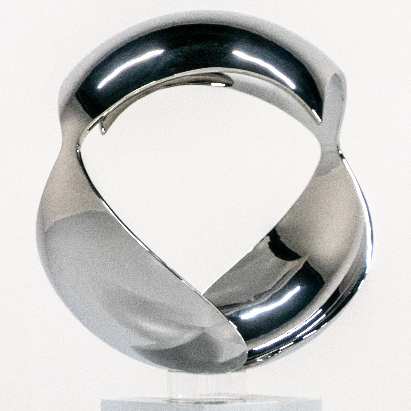 A polished chrome abstract sculpture of two interlocking curved forms mounted on a rectangular white pedestal, photographed in a clean white studio setting.