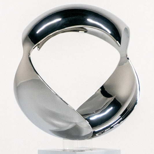 A polished chrome abstract sculpture of two interlocking curved forms mounted on a rectangular white pedestal, photographed in a clean white studio setting.